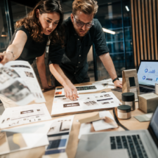 Zwei Personen planen an einem Tisch den Relaunch eines Online-Shops mit Skizzen, Produktverpackungen und anonymen Analyseansichten.