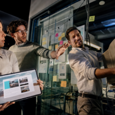 Ein Unternehmerteam plant dynamisch den Relaunch einer veralteten Website mit Skizzen, Tablet und modernem Bürolicht.